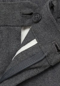 Fodera della cintura di pantaloni in tessuto grigio con un bottone nero, foderatura interna bianca e una texture sottile. Presenta una zip nascosta e un piccolo passante per la cintura.