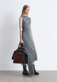 Graues, tailliertes Kleid mit asymmetrischem Ausschnitt, braune Ledertasche und grauer Strickschal; das Modell trägt klobige Schnürstiefel.