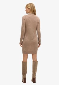 Vestito lungo color cammello a maniche lunghe realizzato in tessuto jersey, caratterizzato da una forma aderente e dettagli a costine sull'orlo, abbinato a stivali alti in pelle scamosciata.