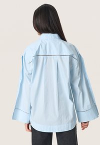 Lichtblauwe katoen shirt met een kraag, lange mouwen en uitsnijdetails langs de achterkant van de schouderpas. Heeft een rechte zoom en knoopmanchetten.
