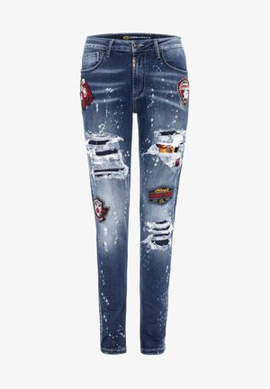 Slim-Fit blaue Jeans aus Denim mit einem abgetragenen Finish, das mehrere Risse und bestickte Patches in Rot und Schwarz aufweist. Akzente setzen Farbspritzer.