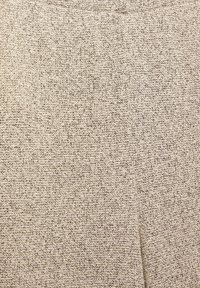 Tissu beige clair avec un motif tissé texturé. Le matériau semble doux et légèrement extensible, adapté à une tenue décontractée.