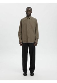 Brun rutete skjorte med knapper, spiss krage, lange ermer og avslappet passform, kombinert med svarte bukser og svarte sko.