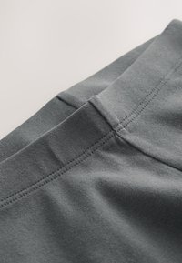 Tela elástica gris con textura suave, que presenta una pretina plana y costuras planas a lo largo de las uniones. Vista en primer plano del material.