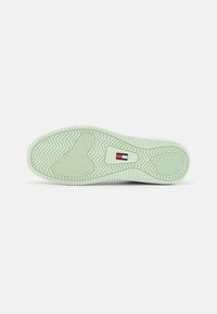 Semelle de chaussure en caoutchouc vert menthe clair avec un motif en zigzag texturé, présentant un petit détail de logo rouge et bleu. Forme plate et arrondie.