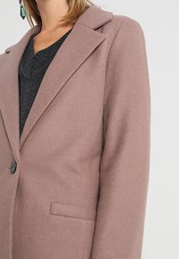 Blush pink uldblandede oversized frakke med klapkrave, to frontlommer og en enkelt knaplukning. Blød tekstur og skræddersyet design.