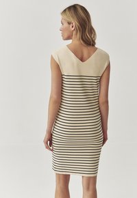 Beige mekko mustilla raidoilla, muotoiltu malli, hihattomat hihat ja V-pääntie takana. Sujuva tekstuuri, polvipituus, minimalistinen tyyli.