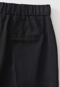 Pantalon en tissu noir avec taille élastique, passants de ceinture et une poche passepoilée au dos, côté droit.