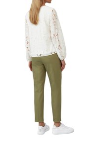 Haut en dentelle blanche avec un motif floral, manches longues et coupe décontractée, associé à un pantalon olive ajusté et des baskets blanches.
