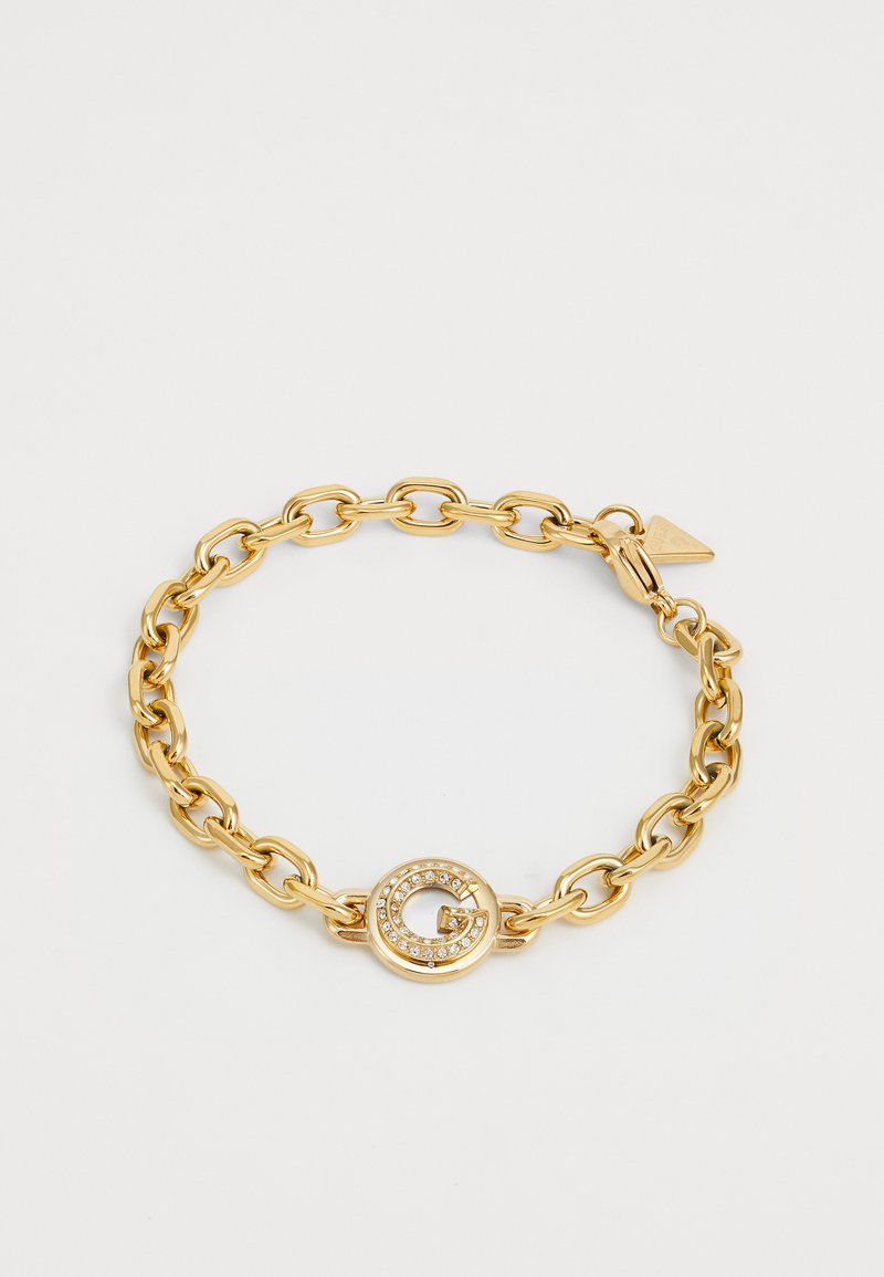 Pulsera de cadena dorada con eslabones grandes y un cierre circular acentuado con gema que presenta un diseño de "G". Textura lisa con acabado brillante.