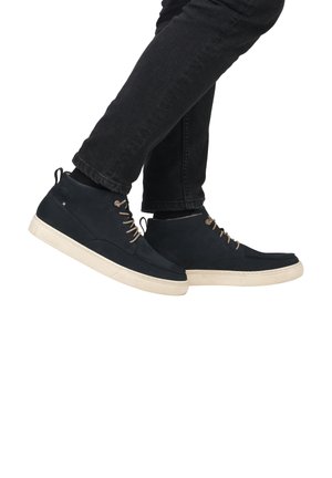 Botas de tobillo de ante azul oscuro con suelas de goma beige claro, que presentan una puntera redonda, cordones en la parte delantera y una lengüeta en la parte posterior para facilitar su calzado.