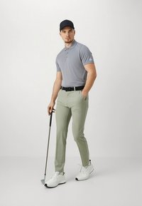 Grå pikétröja, ljusgröna golfbyxor, svart bälte och vita golfsko. Personen håller en golfklubba och bär en marinblå keps.