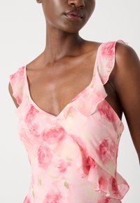Floral-patterned dress in soft pink with ruffled edges along the neckline and shoulder, showcasing a delicate, textured fabric.
