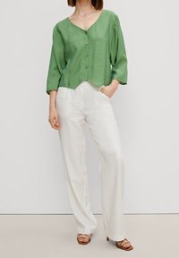 Haut vert à boutons avec un décolleté en V et des manches trois-quarts, associé à un pantalon large blanc et des sandales à talons beiges.