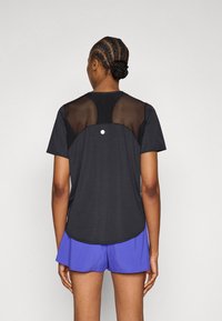 Μαύρο αθλητικό μπλουζάκι με διχτυωτά πάνελ στο άνω μέρος της πλάτης, συνδυασμένο με μπλε σορτς· ομαλή υφή και στρογγυλεμένο τελείωμα.
