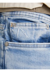 Ljusblå denimjeans har en framficka för mynt med silverfärgade detaljer. Tyget visar bleka områden och subtila slitningar.