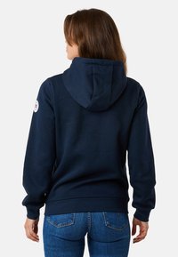 Sweat-shirt bleu marine avec une poche kangourou, des poignets côtelés, une capuche avec cordon de serrage et un logo circulaire sur l'épaule gauche. Le tissu est doux et lisse.