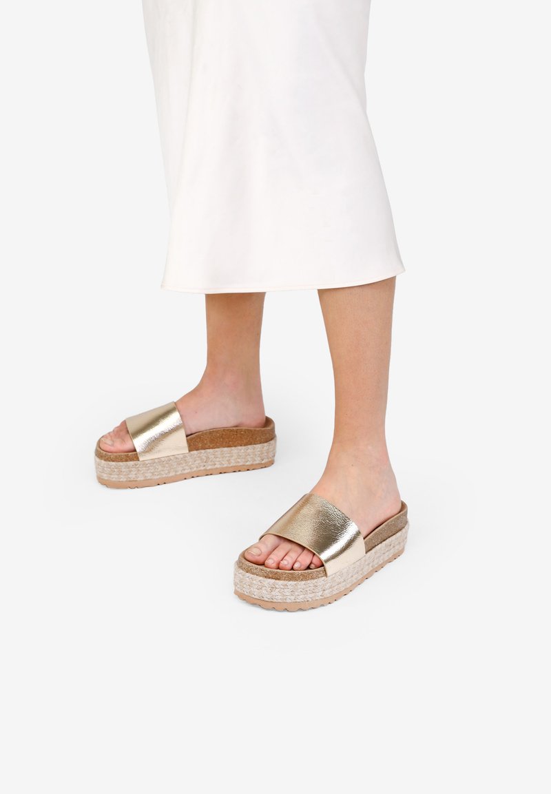 Sandalias de slide metálicas doradas con suela trenzada y plantilla de corcho. Diseño plano, punta abierta y materiales texturizados para mayor agarre.
