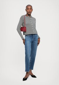 Schwarz-weiß gestreiftes Hemd, blaue gerade Jeans, schwarze spitze Schuhe und eine kleine rote Handtasche. Glatte Texturen, lässiger Look.
