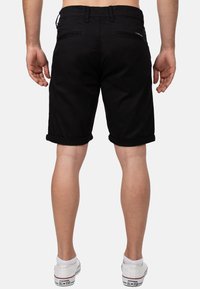 Shorts en denim noir avec des ourlets roulés, poches arrière et une texture lisse vus de l'arrière, associés à des baskets blanches.