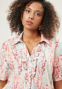 Blusa floreale color azzurro chiaro con motivi rosa e corallo, con dettagli arricciati sul davanti, chiusura con bottoni e maniche corte. Tessuto morbido al tatto.