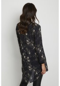 Blusa a manica lunga di un blu scuro con motivi astratti crema e verdi, realizzata in tessuto leggero, con un orlo leggermente curvato.