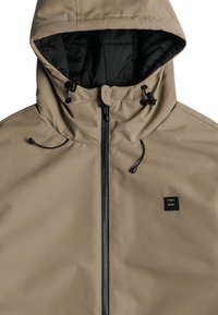 Beige vattentät jacka med dragkedja fram, snodd i huvan och svart innerfoder. Har en liten svart logotyp på bröstet.