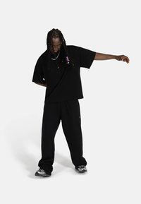 Preveliki crni majica s grafičkim detaljem, uparen s crnim trenirkama. Sive tenisice upotpunjuju monohromatski outfit.