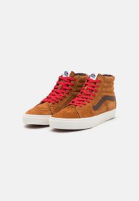 Zapatillas altas de ante marrón con cordones rojos, que presentan suelas de goma blanca y una franja lateral marrón. Texturizadas, con un collar acolchado.