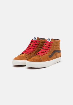 Hoge sneakers van bruin suede met rode veters, met witte rubberen zolen en een bruine zijstreep. Textuur, met een gewatteerde kraag.