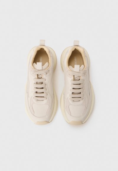 Beige sneakers with a smooth leather upper, rounded toe, and textured outsole. Features a lace-up design and soft padded collar.
