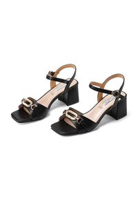 Sandali neri in pelle con tacco quadrato e punta quadrata, con accenti di catene dorate e cinturini alla caviglia regolabili. Texture liscia e design elegante.