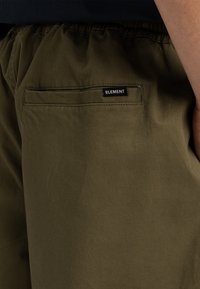 Olivgrüne Shorts aus strapazierfähigem Stoff, mit einem elastischen Bund und einer Gesäßtasche mit einem schwarzen "ELEMENT"-Label.