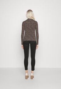 Top de manga larga y corte ajustado con un patrón de puntos multicolores sobre un fondo oscuro, combinado con jeans skinny negros y tacones bajos destalonados.