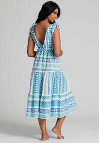 Ärmlös maxiklänning i blått och vitt med V-back, som har geometriska mönster och volangaxlar, tillverkad av lättviktsmaterial.
