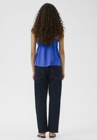 Modra brezrokavna majica iz lahkega materiala, ohlapnega kroja; temno modri jeans z visokim pasom, ravnega kroja, z minimalnimi šivi, ravni sandal.