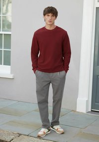 Bordeauxrotes langärmeliges Hemd, kombiniert mit hellgrauen Hosen und mehrfarbigen Sneakers. Der Stoff wirkt glatt und hat eine lässige Passform.