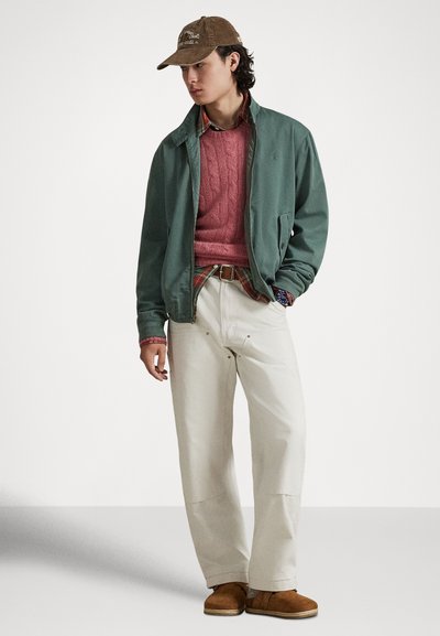 Πράσινο μπουφάν με φερμουάρ, ροζ πλεκτό πουλόβερ με σχέδιο κοτσίδας, πουκάμισο καρό, κρεμ παντελόνι με φαρδιά πόδια και καφέ παπούτσια χωρίς κορδόνια. Το καπέλο διαθέτει κεντημένο λογότυπο.