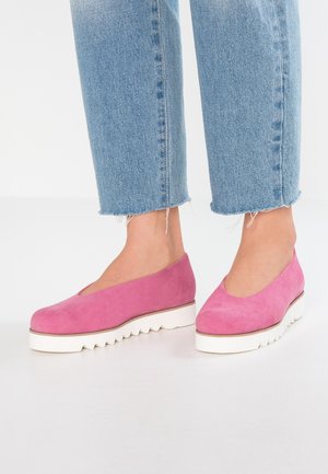 Chaussures en suède rose avec un bout rond et une semelle blanche ondulée. Les chaussures s'élèvent légèrement au-dessus de la cheville, associées à un jean bleu court.