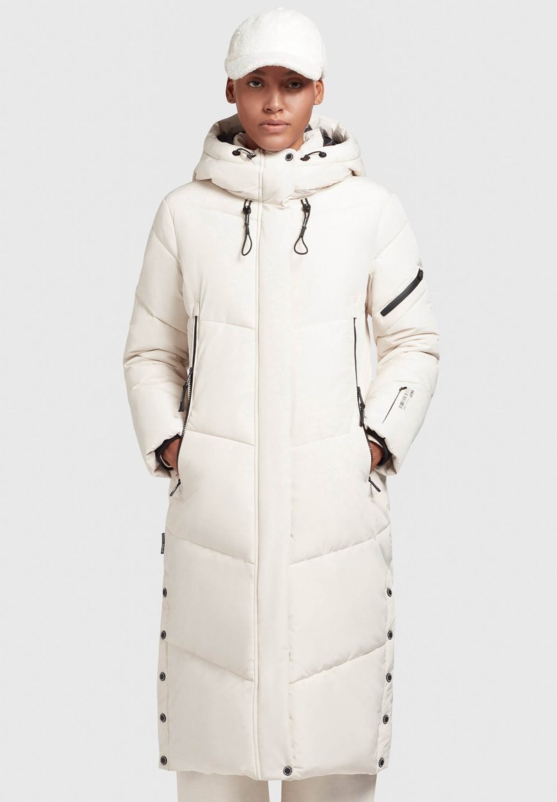 Manteau long blanc matelassé avec capuche, comprenant une poche zippée, un détail de côté boutonné, et un motif matelassé diagonal. Design chaud et isolé.