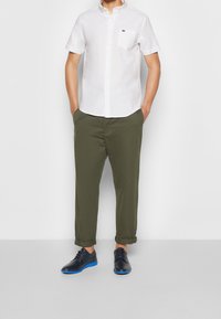 Biała koszula z krótkim rękawem, zapinana na guziki, z kieszenią na piersi, zestawiona z oliwkowymi spodniami i czarnymi butami z niebieską podeszwą.