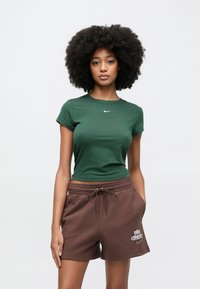 Πράσινο βαμβακερό t-shirt με κοντά μανίκια και λευκό λογότυπο, συνδυασμένο με καφέ βαμβακερά σορτς που έχουν λευκό γραφικό σχέδιο.