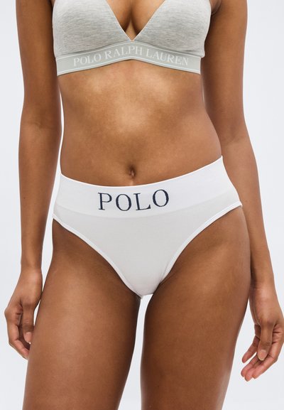 Femme portant un bralette gris Polo Ralph Lauren et une culotte taille haute blanche avec le logo "POLO" sur la ceinture, debout devant un fond uni.