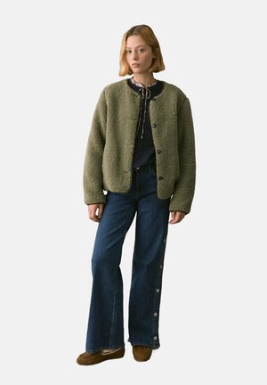 Green, plush, fleece jacket with a round neckline and button closure. Paired with wide-leg dark denim jeans featuring side button accents.