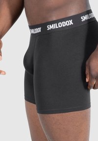 Svarta boxershorts i mjukt tyg med en svart midja som har vit "SMILODOX"-logotyp. Tight passform.