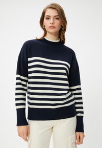 Marineblauwe en crèmekleurige gestreepte trui met een hoge hals, zachte textuur, verlaagde schouders en geribbelde boorden, tegen een effen achtergrond.