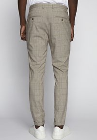 Harmaat ruudulliset housut, joissa on räätälöity istuvuus ja takataskut kultanapeilla. Yhdistettynä valkoisiin lenkkareihin.