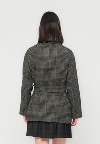 Black and white houndstooth patterned blazer with a cinched waist, long sleeves, and a structured back. Smooth fabric with slight sheen.