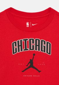 Camiseta de algodón roja con la palabra "CHICAGO" en negro y un contorno gris, además de una silueta negra de un jugador de baloncesto saltando. Incluye los logotipos de la NBA y de Nike.