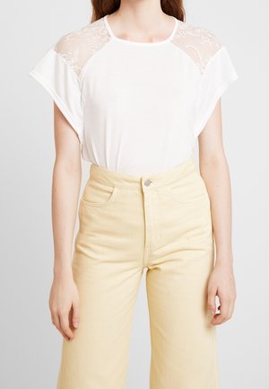 T-shirt bianco con dettagli in pizzo sulle spalle, maniche corte e scollatura rotonda, abbinato a pantaloni gialli a vita alta con tasche.